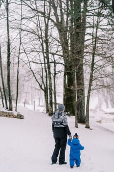 Mom with a small child stands in a snowy forest and looks into the distance. Back view. High quality photo