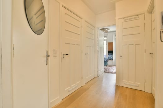 a long hallway with white doors and wood flooring on either side by side, looking into the living room