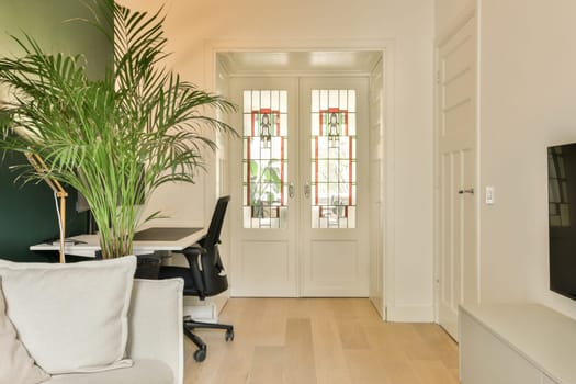 a living room with a plant in the corner and an office chair on the floor next to the door,