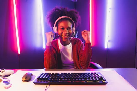 Gaming streamer, African girl playing online fighting with Esport skilled team wearing headphones in neon color lighting room. Talking other players planing strategies to win competitors. Tastemaker.