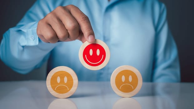 Concepts of mental health and emotional states. A person chooses a smiley face instead of a sad face on a piece of wood to represent the concept of choosing positive thinking.