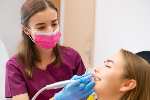 Professional woman dentist doctor doing professional cleaning of teeth to the patient.