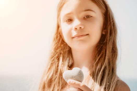 Female hand holding a stone in the shape of a heart against the background of the sea