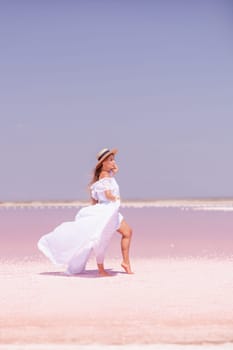 Woman in pink salt lake. She in a white dress and hat enjoys the scenic view of a pink salt lake as she walks along the white, salty shore, creating a lasting memory