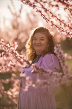 Woman blooming peach orchard. Against the backdrop of a picturesque peach orchard, a woman in a long pink dress and hat enjoys a peaceful walk in the park, surrounded by the beauty of nature