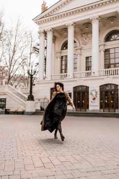 Woman street lifestyle. Image of stylish woman walking through European city on sunny day. Pretty woman with dark flowing hair, dressed in a beige raincoat and black, walks along the building