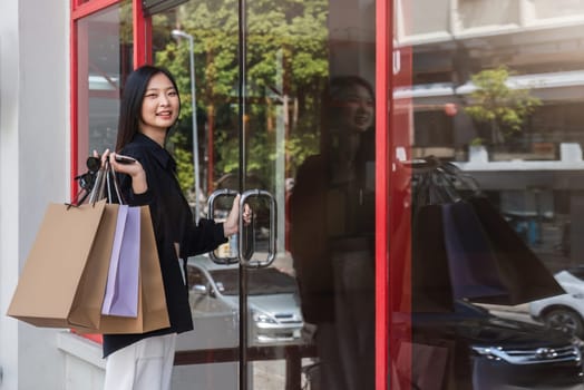 Asian woman using smartphone and looking away while enjoying a day shopping. Black Friday sale and discount. Buying clothes presents for holidays.