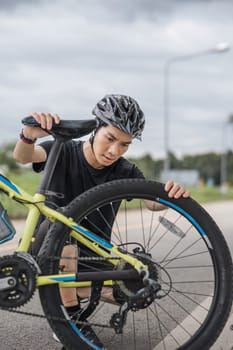 A professional young Asian male cyclist fix his bike chain on the street after riding on country roads. maintenance, repair.