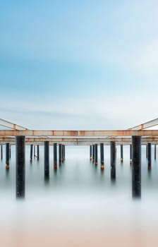 Fine art view of columns under metal pier at sunrise. Shot with long exposure to make the sea appear as fog