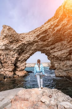 woman sea travel. A woman in a blue jacket stands on a rock above a cliff above the sea, looking at the stormy ocean. Girl traveler rests, thinks, dreams, enjoys nature.