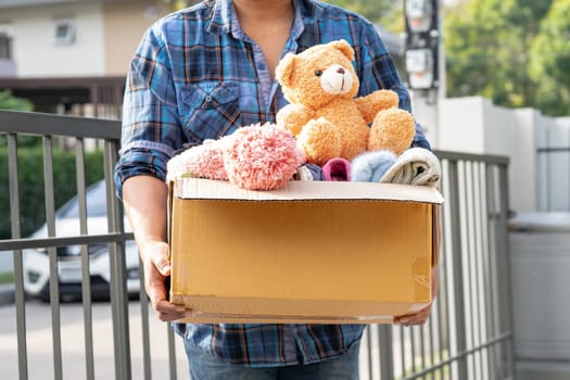 Volunteer woman provide clothing donation box with used clothes and doll to support help for refugee, homeless or poor people in the world.