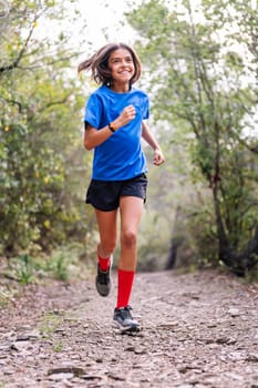 smiling girl practicing trail running in the forest, concept of sport in nature and healthy lifestyle for children