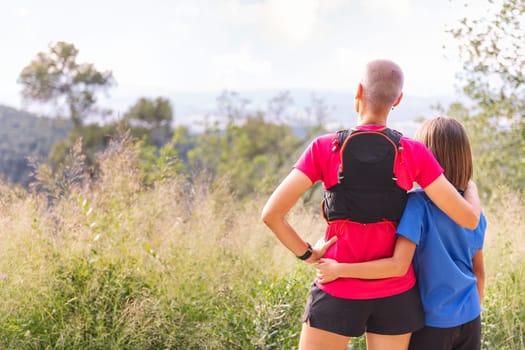 rear view of a woman with her daughter looking at the landscape after doing sports in the countryside, concept of active lifestyle and sport with kids in the nature, copy space for text