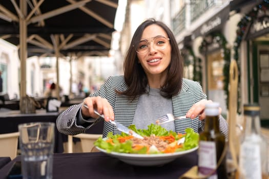 Business woman in glasses eating salad at cafe table. Beautiful middle age female enjoying fresh salad at nice restaurant.