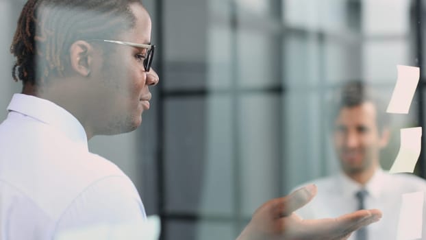 two businessmen discussing business strategy. standing behind the glass looking at stickers.