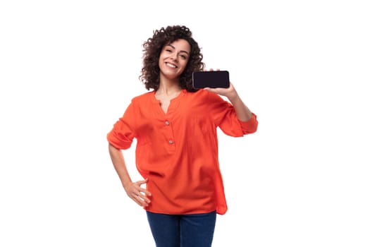 young curly brunette lady dressed in a stylish bright orange shirt shows the smartphone screen.