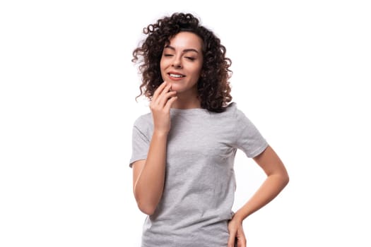 authentic cute slim curly woman with black hair dressed in casual gray t-shirt on white background with copy space.