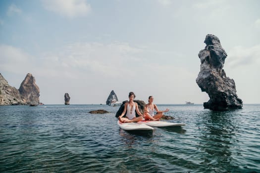 Woman sup yoga. Middle age sporty woman practising yoga pilates on paddle sup surfboard. Female stretching doing workout on sea water. Modern individual hipster outdoor summer sport activity