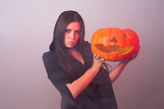 Gothic young woman in witch halloween costume with a carved pumpkin.