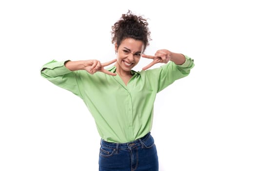 young positive brunette businesswoman with curly hair tied up in a ponytail in a light green shirt in a studio space.