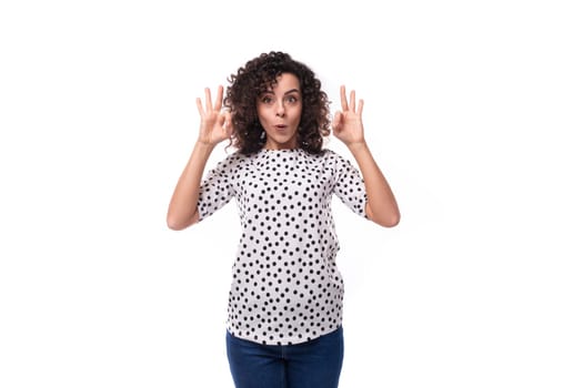 young surprised well-groomed brunette curly woman dressed in a polka dot print blouse.