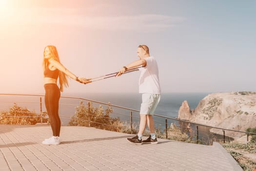 Happy Middle aged couple or friends practicing nordic walking in park near sea. Mature couple with trekking poles walking, practicing Nordic walking outdoors. Aging youthfully and sport concept.