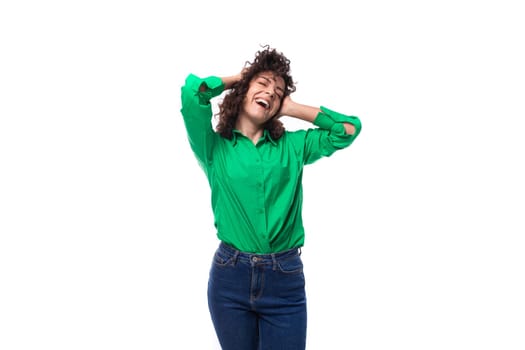 young stylish caucasian brunette woman with curled hair dressed in a green shirt posing on a white background with copy space.