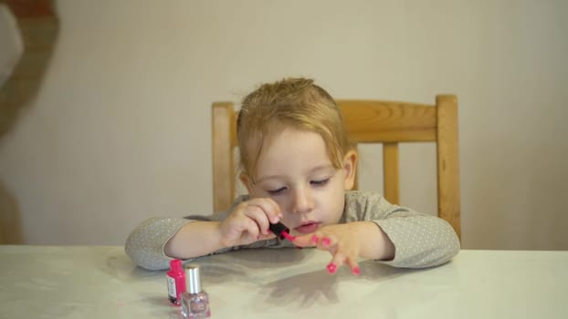 A little girl paints her nails with pink polish. The girl, having put on her makeup, blows on her nails to let them dry. 4k