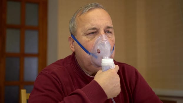 An elderly man inhales through an oxygen mask. A man does a respiratory procedure at home. Closeup. 4k