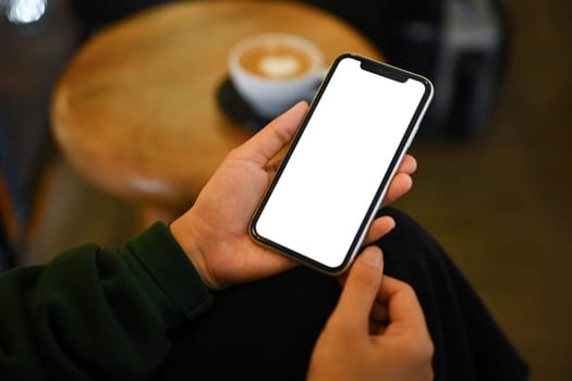 Young woman hands holding smartphone with blank screen while sitting at modern coffee shop.
