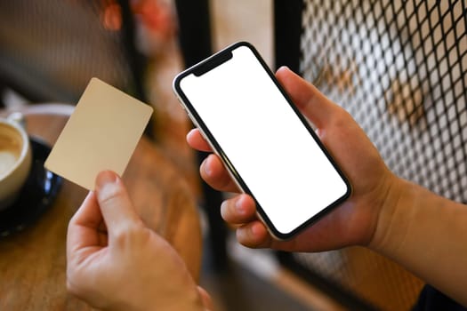 Close up man holding credit card and smartphone entering information or ordering in internet store.