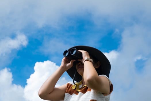 Young woman with binoculars on the mountain on a sunny day. Woman using binoculars when going hiking. Hiking woman uses binoculars to travel and has a happy smile.