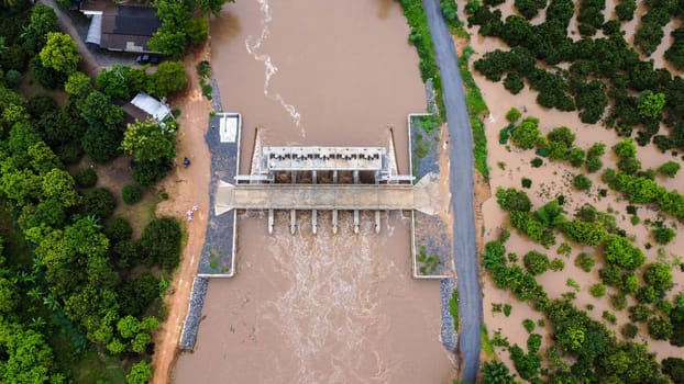 Aerial view of water released from the drainage channel of the concrete dam is a way of overflowing water in the rainy season. Top view of turbid brown forest water flows from a dam in Thailand.