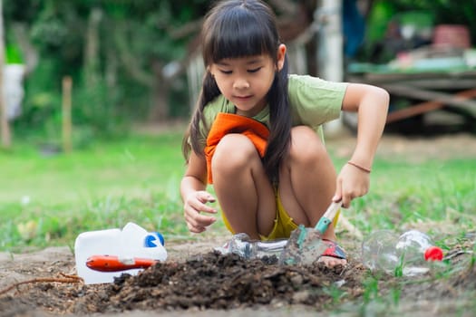 Little girl planting plants in pots from recycled water bottles in the backyard. Recycle water bottle pot, gardening activities for children. Recycling of plastic waste