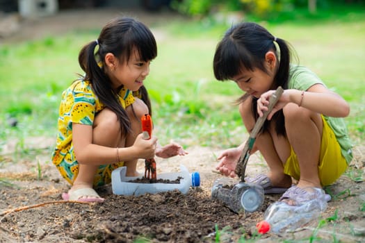 Little girl planting plants in pots from recycled water bottles in the backyard. Recycle water bottle pot, gardening activities for children. Recycling of plastic waste