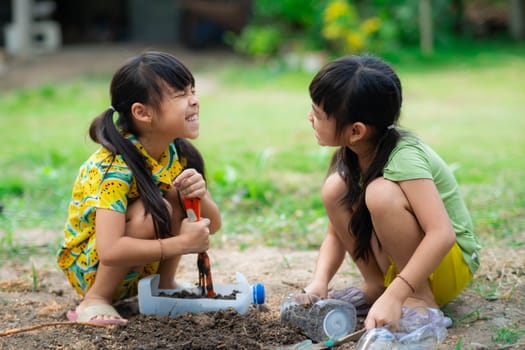 Little girl planting plants in pots from recycled water bottles in the backyard. Recycle water bottle pot, gardening activities for children. Recycling of plastic waste