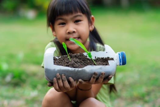 Little girl shows saplings grown in recycled plastic bottles. Recycle water bottle pot, gardening activities for children. Recycling of plastic waste