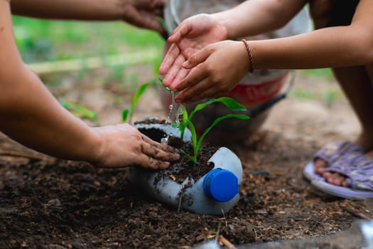 Little girl and mom grow plants in pots from recycled water bottles in the backyard. Recycle water bottle pot, gardening activities for children. Recycling of plastic waste