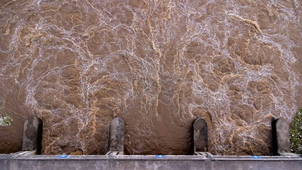 Aerial view of water released from the drainage channel of the concrete dam is a way of overflowing water in the rainy season. Top view of turbid brown forest water flows from a dam in Thailand.