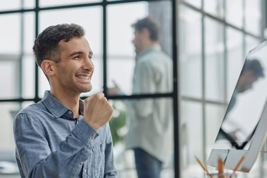 Excited modern businessman sitting at office desk and rejoicing his success