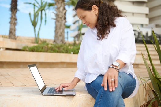 Beautiful curly haired brunette, business woman, planning new startup project on laptop, remotely working outdoor. People. Career. Recruitment. Online business. Education and internet learning