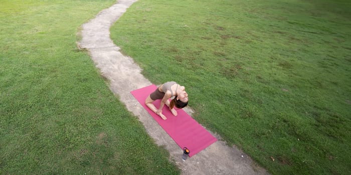 Asian woman sporty practicing yoga at public park outdoor, stretching her body. Healthy active lifestyle.