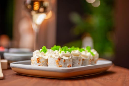 Sushi roll with cream cheese, sesame seeds and green flying fish caviar on a plate close-up. High quality photo