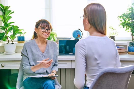 Young female at therapy meeting with psychotherapist. Session of teenage student girl, psychologist with clipboard talking to patient. Psychology, psychotherapy, treatment, youth mental health