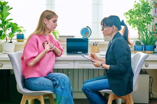 Young female at therapy meeting with psychotherapist. Session of teenage student girl, psychologist with clipboard talking to patient. Psychology, psychotherapy, treatment, youth mental health