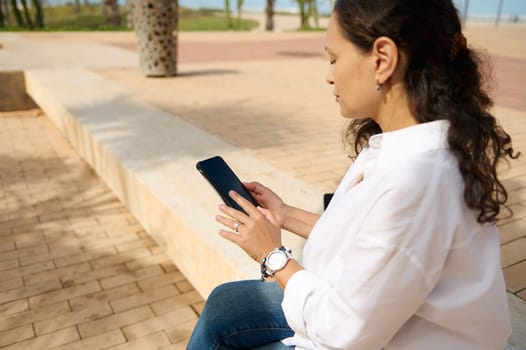 Rear view of a business woman in white shirt, using smartphone and tapping screen while chatting online, booking, ordering. Copy space for mobile application. People. Connection. Online communication.