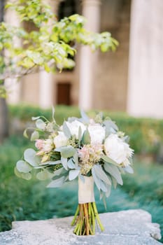 Bouquet of flowers stands on an antique stone pedestal in the garden. High quality photo