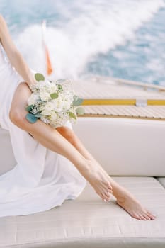 Bride with a bouquet sits on board a yacht sailing on the sea. Cropped. Faceless. High quality photo