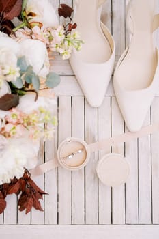 Wedding rings in a box stand on the table near the bride shoes and a bouquet of flowers. Top view. High quality photo