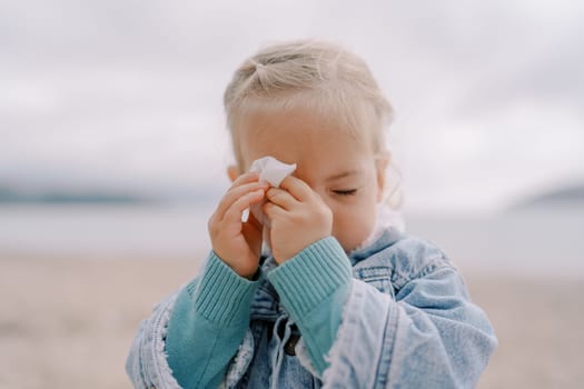 Little girl with closed eyes wipes her forehead with a napkin. High quality photo